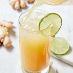 A glass decorate with a slice of lime being filled from a pitcher of Jamaican ginger beer