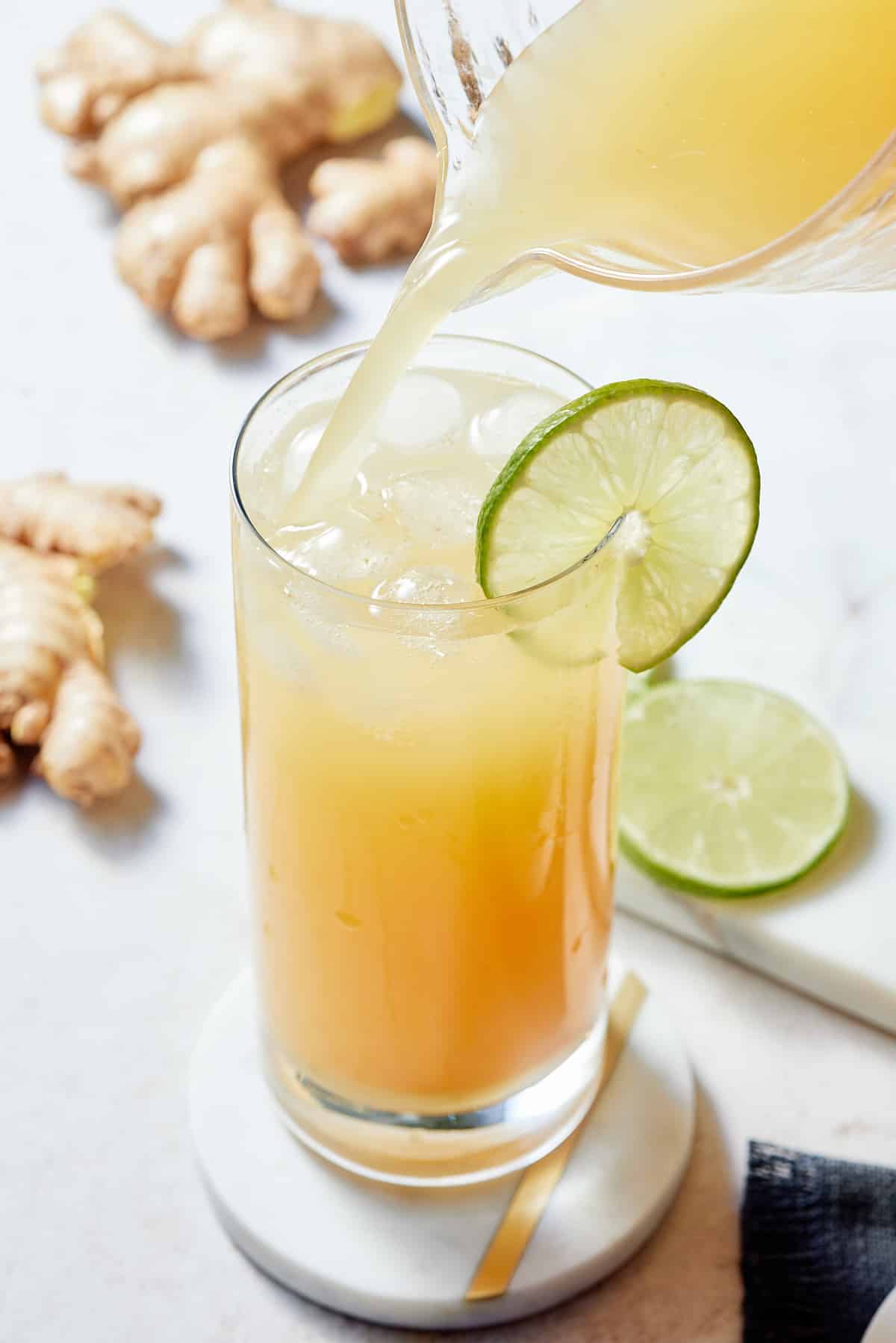 A glass decorate with a slice of lime being filled from a pitcher of Jamaican ginger beer