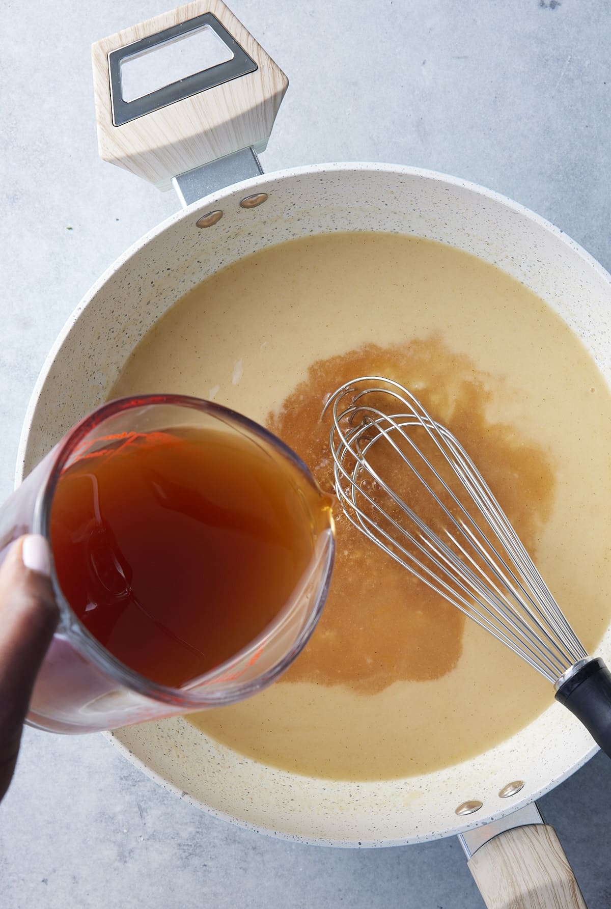 Large skillet with beef and chicken broth being whisked into gravy base