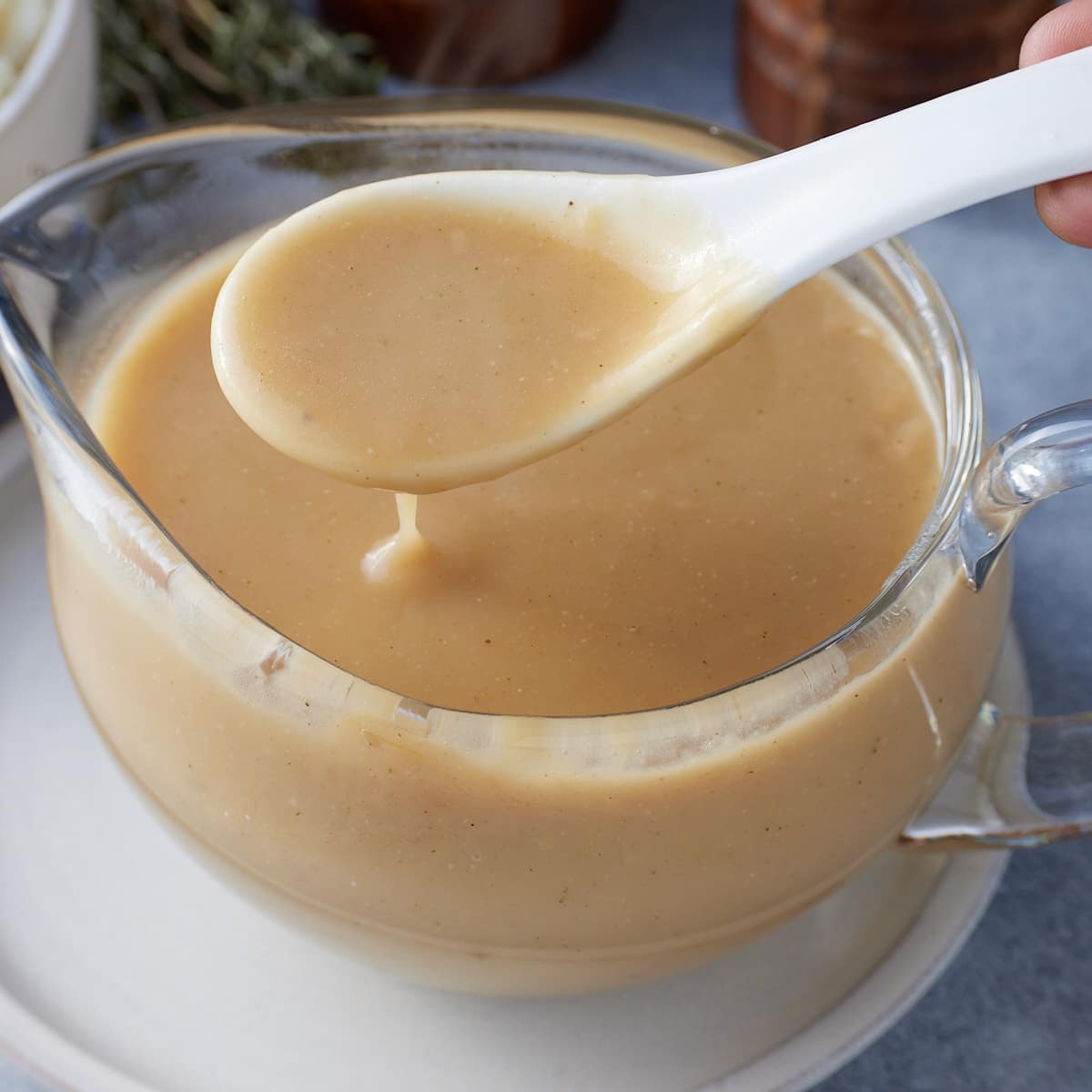 A glass gravy jug filled with brown gravy and a white ceramic spoon