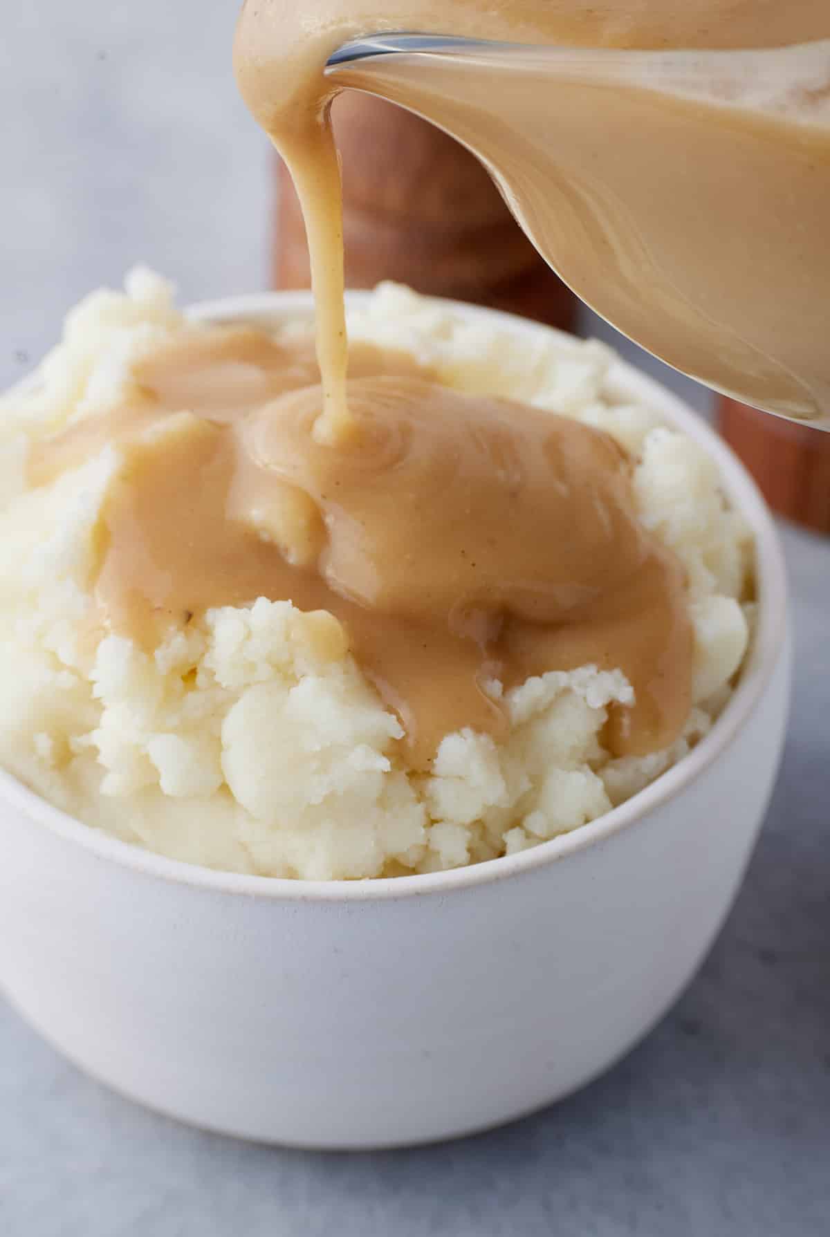 Brown gravy being poured over a bowl of mashed potatoes