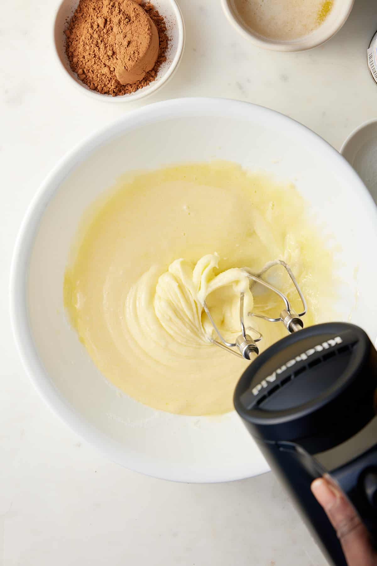 Eggs and granulated sugar being beaten together in a large white bowl with an electric mixer