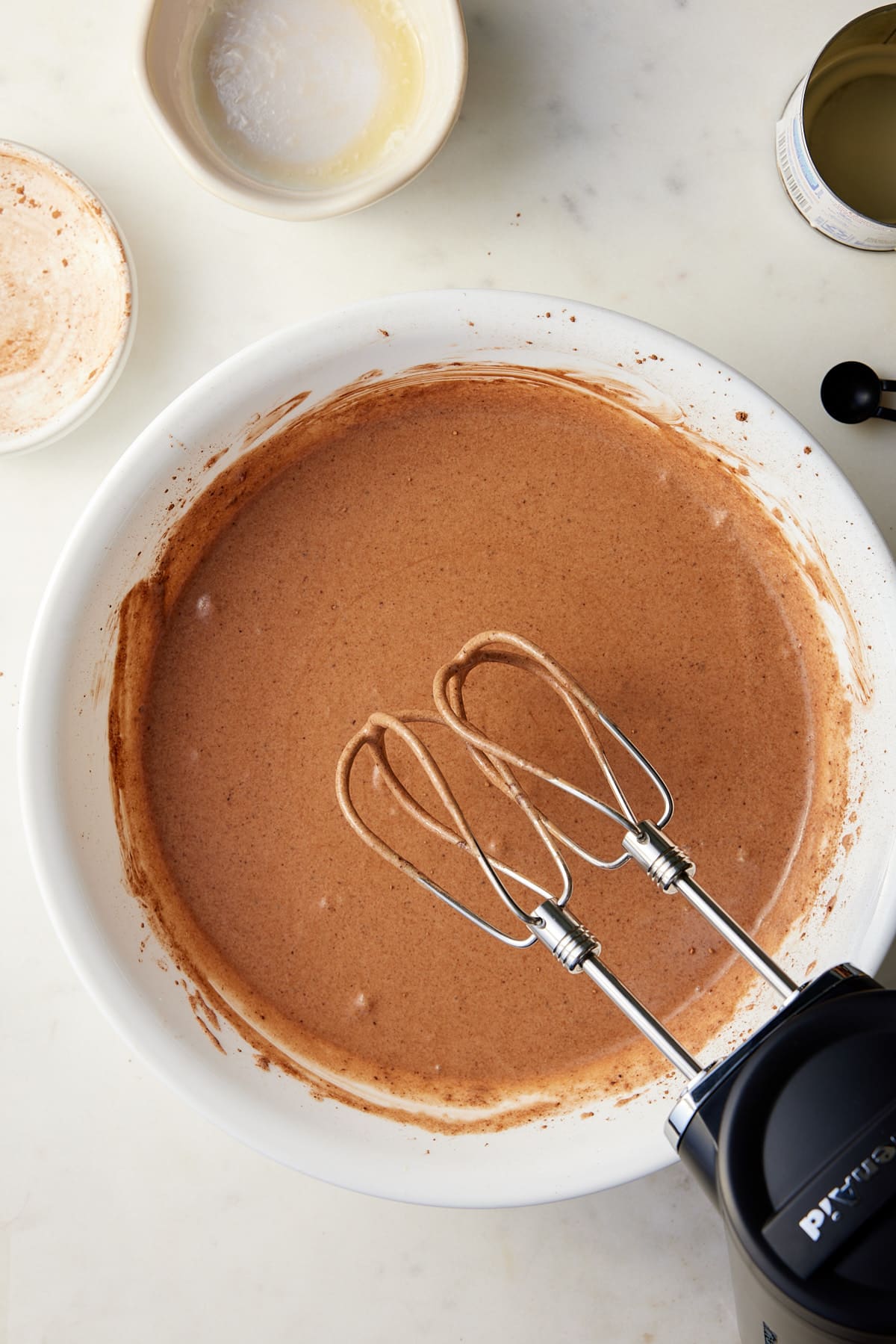 A large white bowl with the ingredients for chocolate chess pie filling being beaten together with an electric mixer