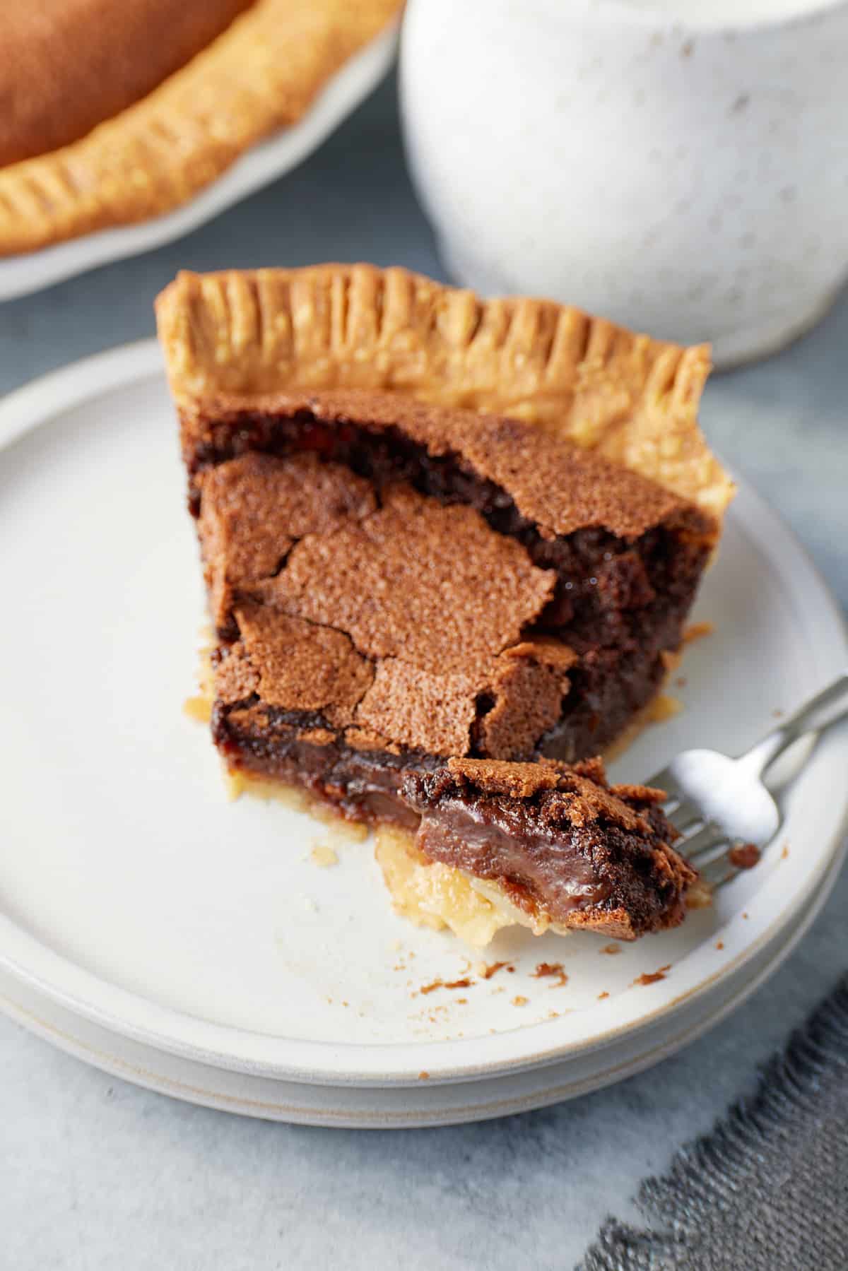 A slice of chocolate chess pie on a plate and a fork with a piece of pie on it