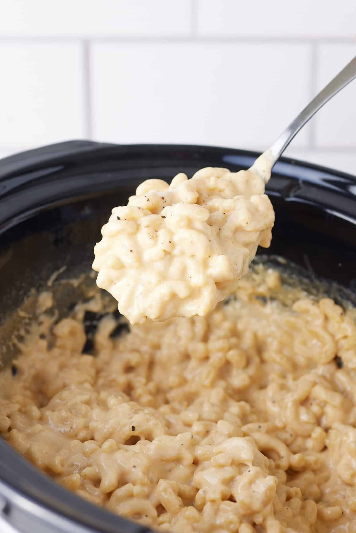 a spoon full of mac and cheese taken from the slow cooker