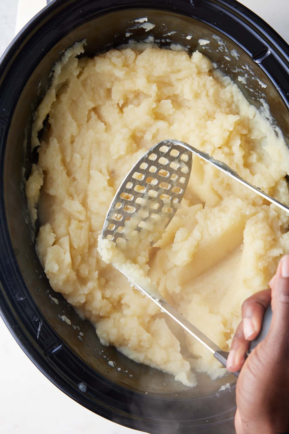 creamy mashed potatoes in a slow cooker being mashed