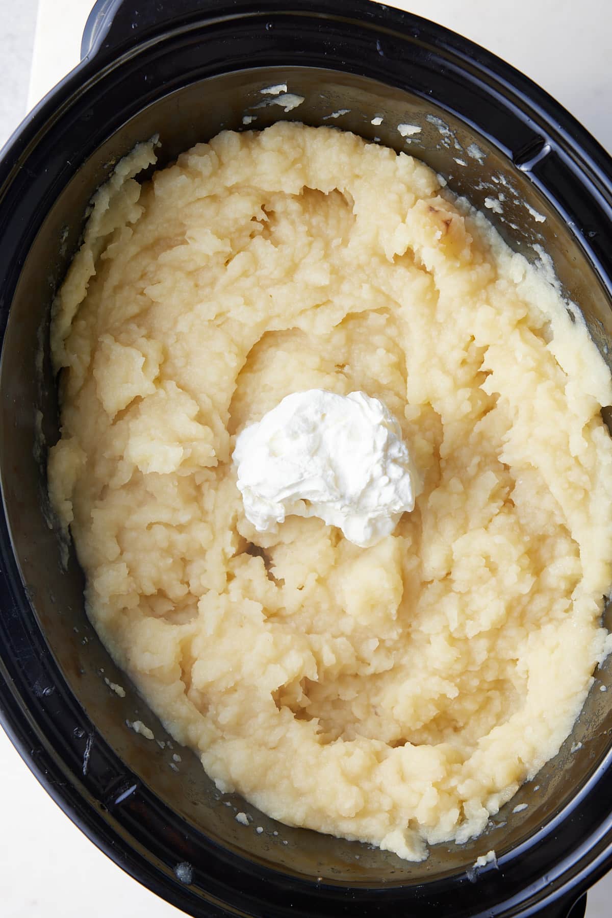 creamy mashed potatoes in a slow cooker with sour cream on top