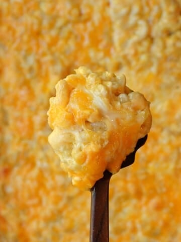 A serving spoon lifting a creamy scoop of mac and cheese from the baking dish.