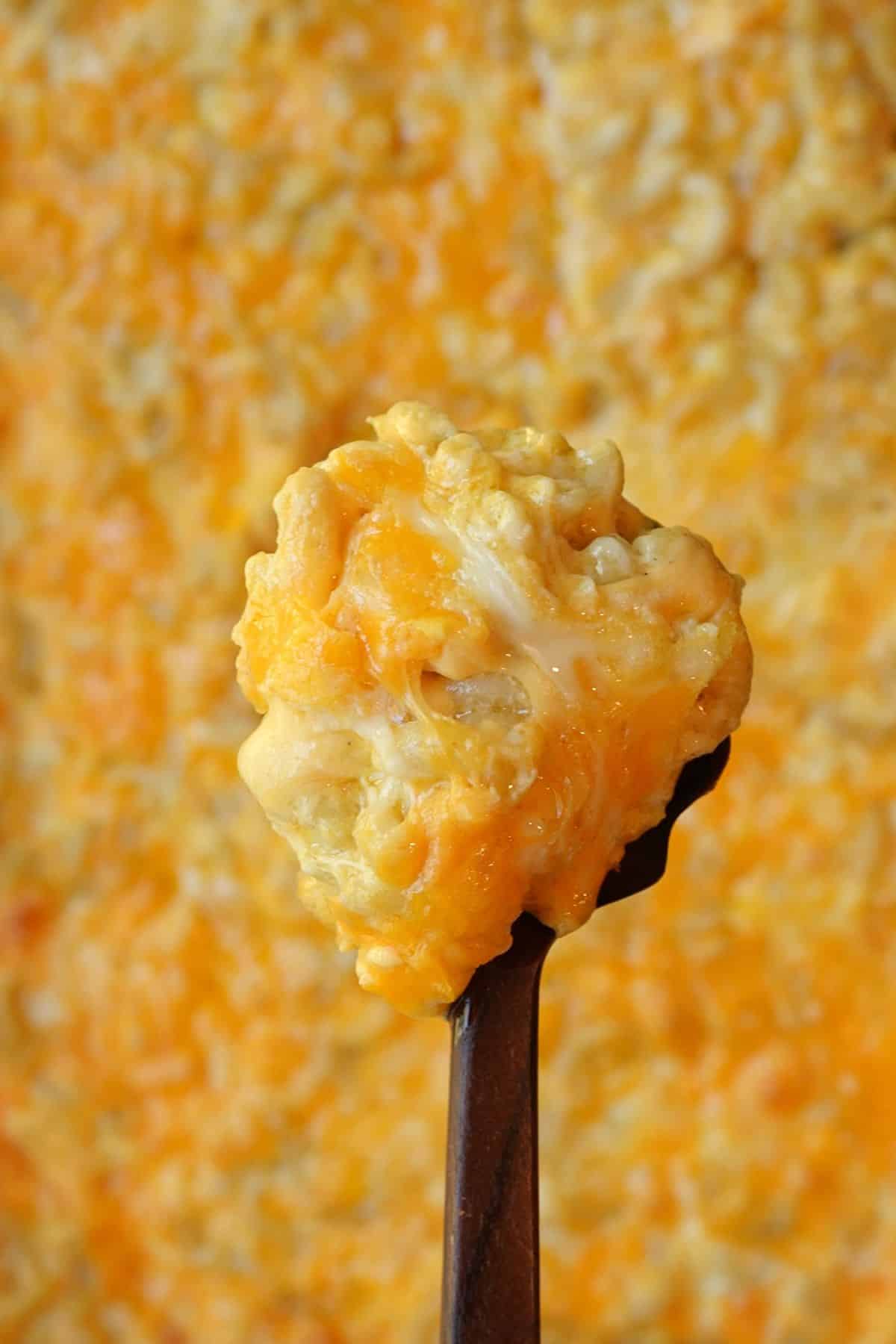 A serving spoon lifting a creamy scoop of mac and cheese from the baking dish.