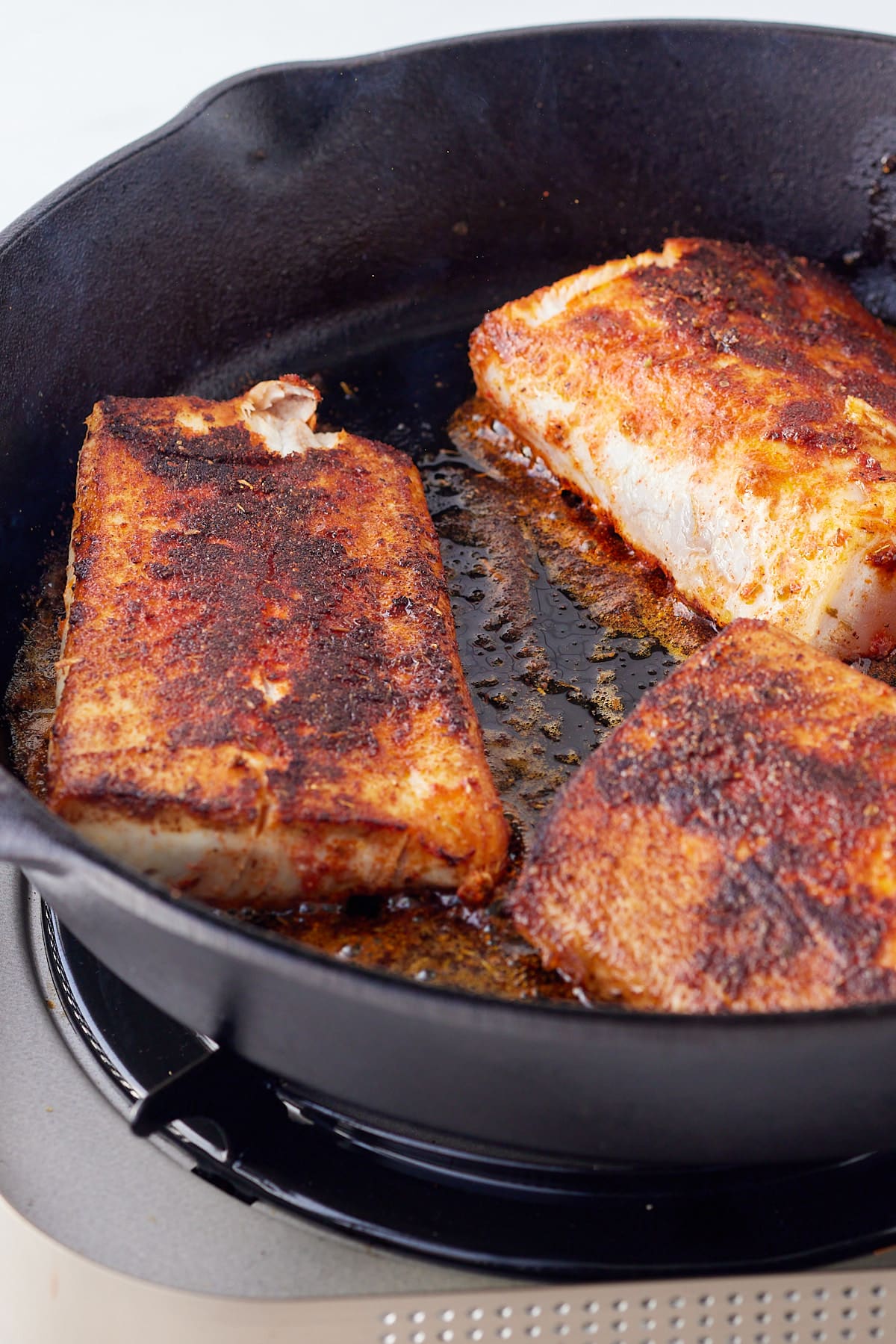 blackened mahi mahi being cooked in a cast iron pan