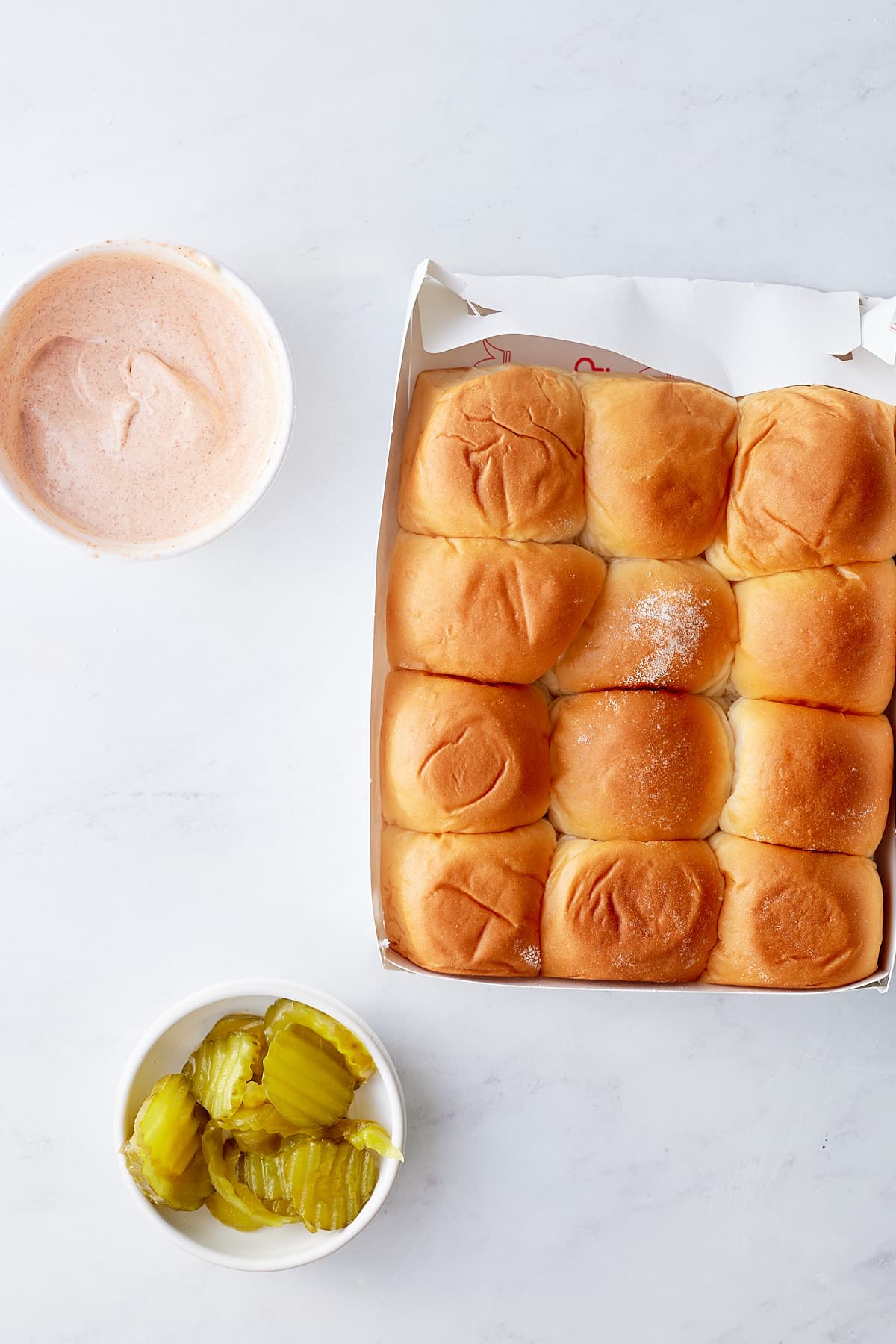 dinner rolls, spicy mayo, and pickles on white background