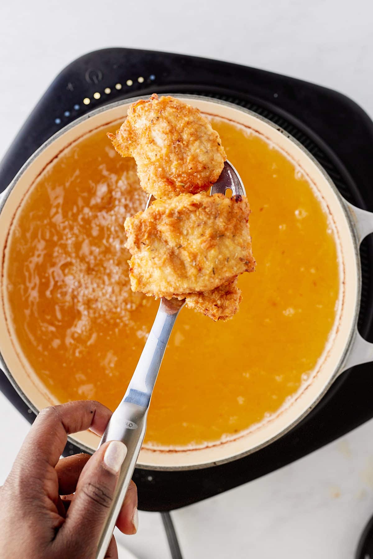 fried chicken being pulled out of oil with spoon