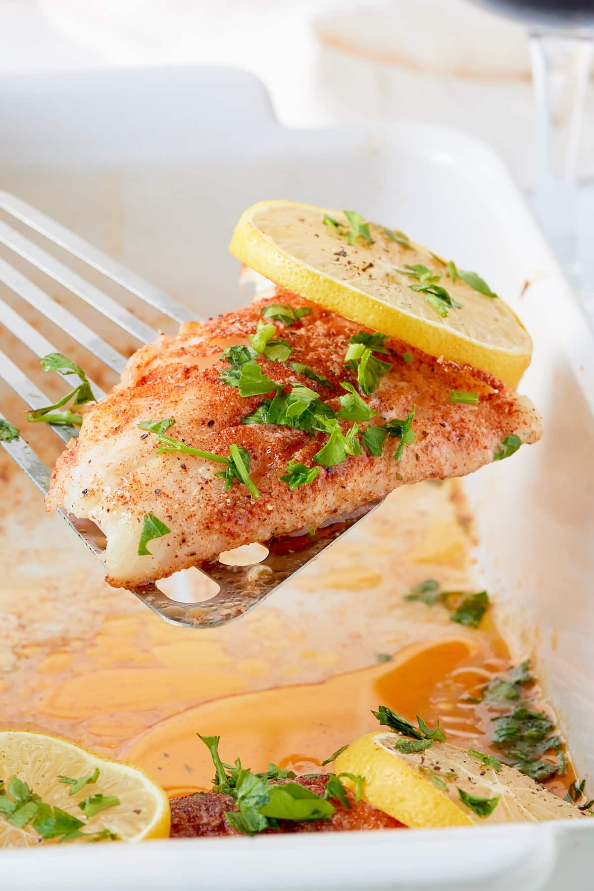 a spatula picking up a piece of oven baked cod topped with lemon