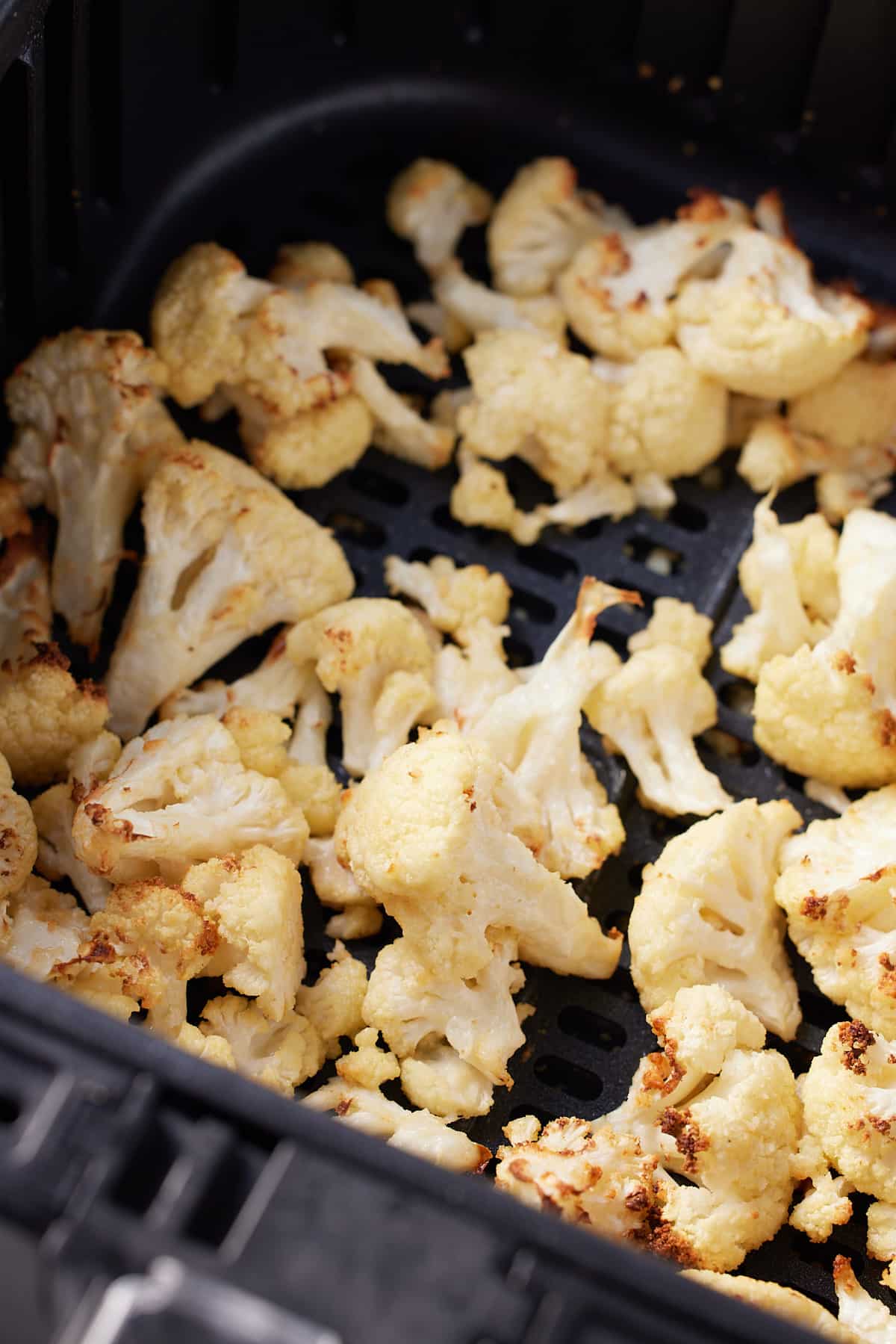 close up image of roasted cauliflower florets in air fryer basket