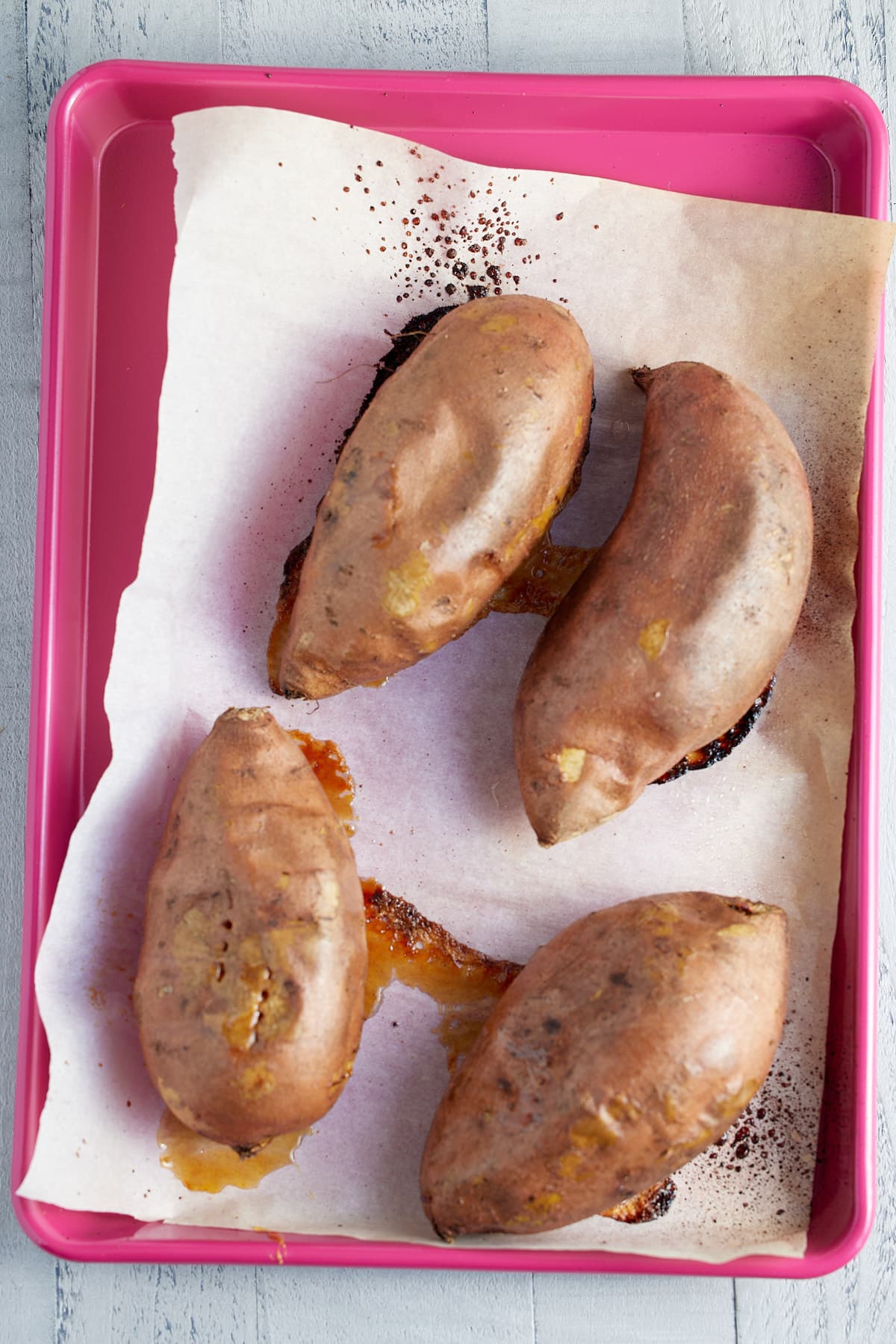 four baked sweet potatoes on a pink baking tray lined with baking parchment