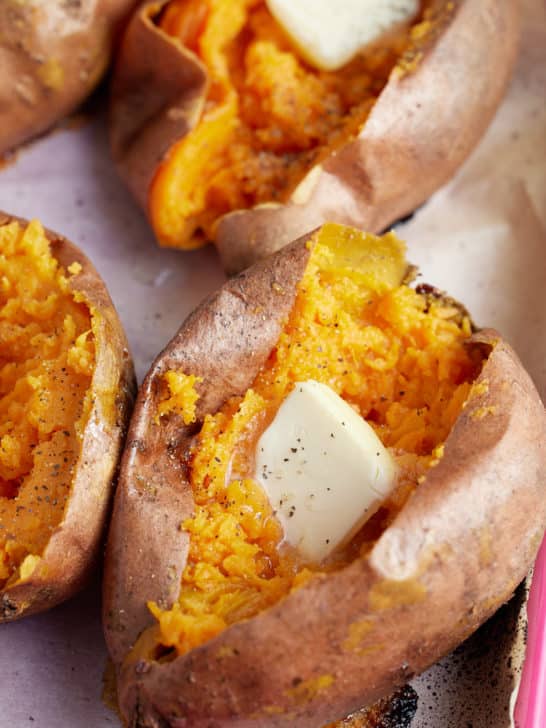 close up image of oven baked sweet potatoes topped with butter and seasoning