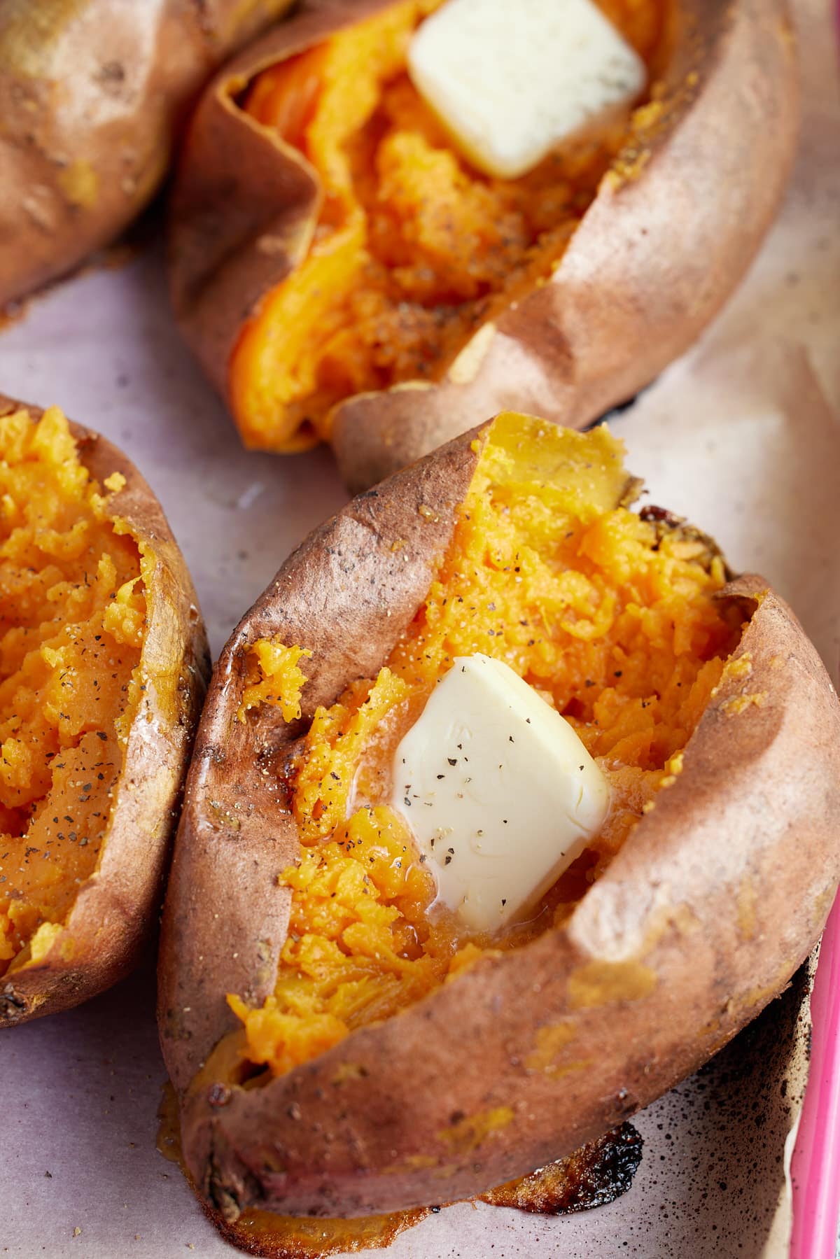 close up image of oven baked sweet potatoes topped with butter and seasoning