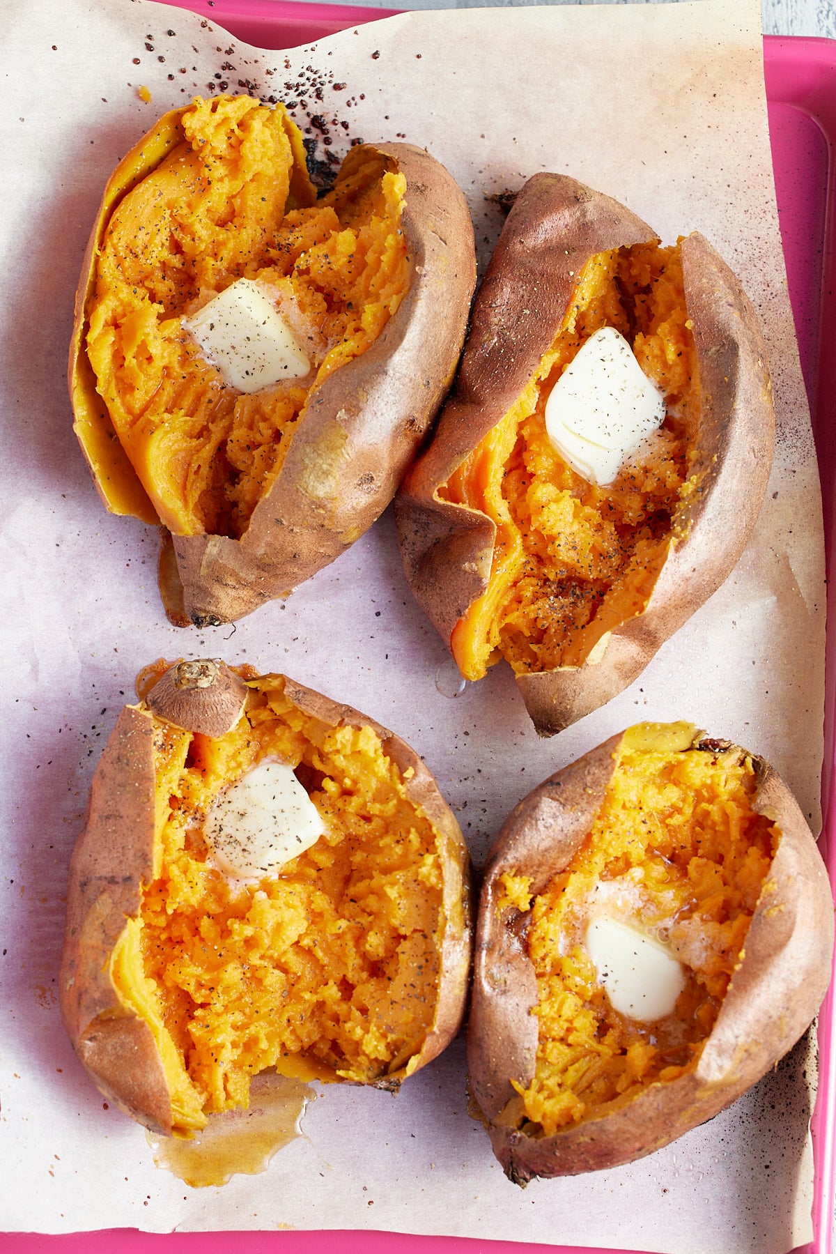 four baked sweet potatoes topped with butter and seasoning