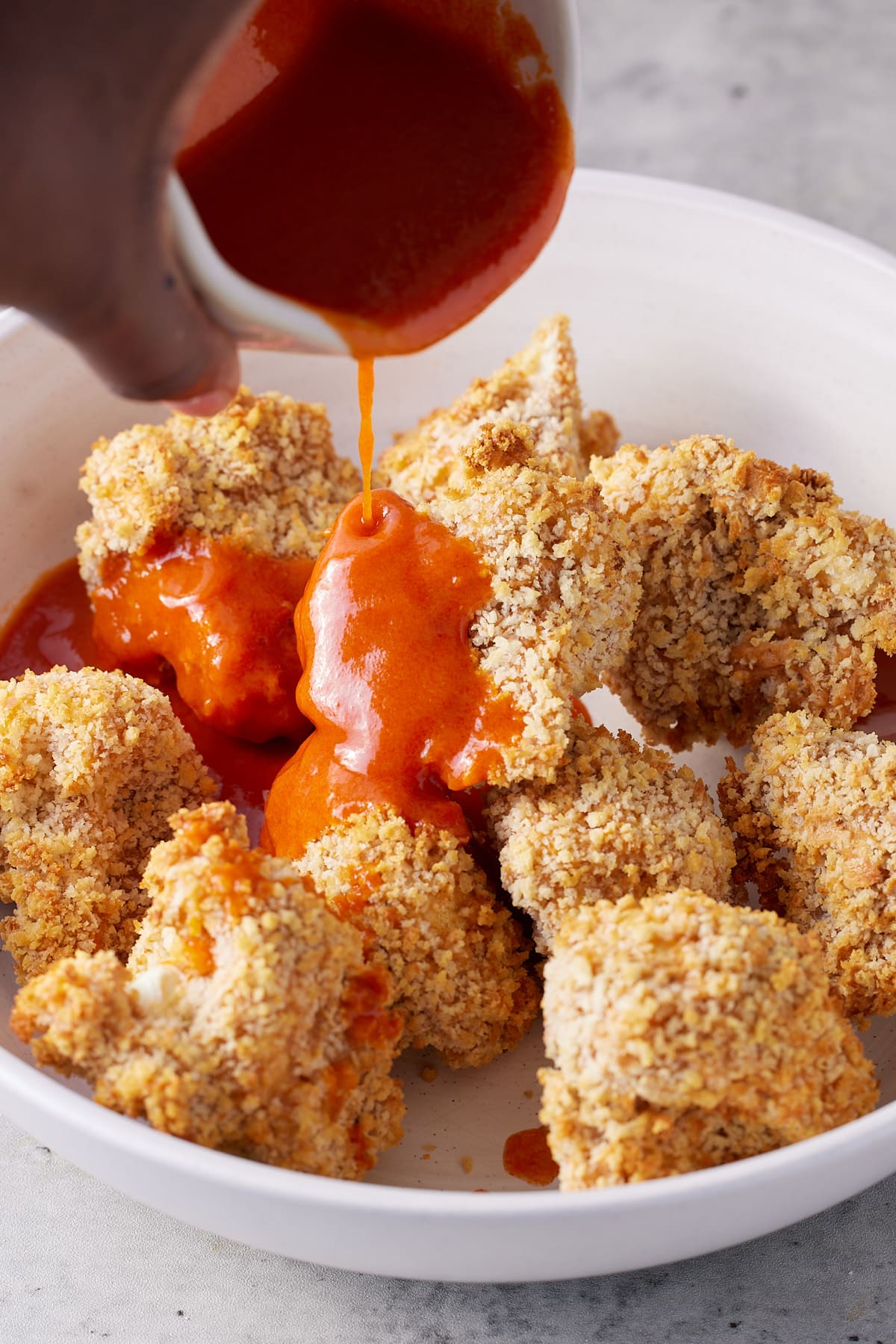 jug of buffalo sauce being poured over fried cauliflower wings