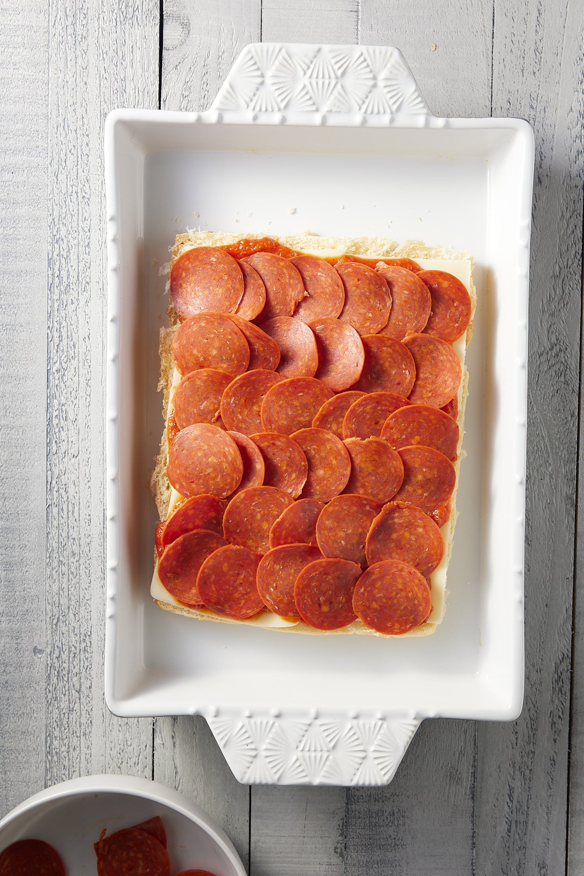 white oven proof dish with base of bread rolls topped with slices of pepperoni