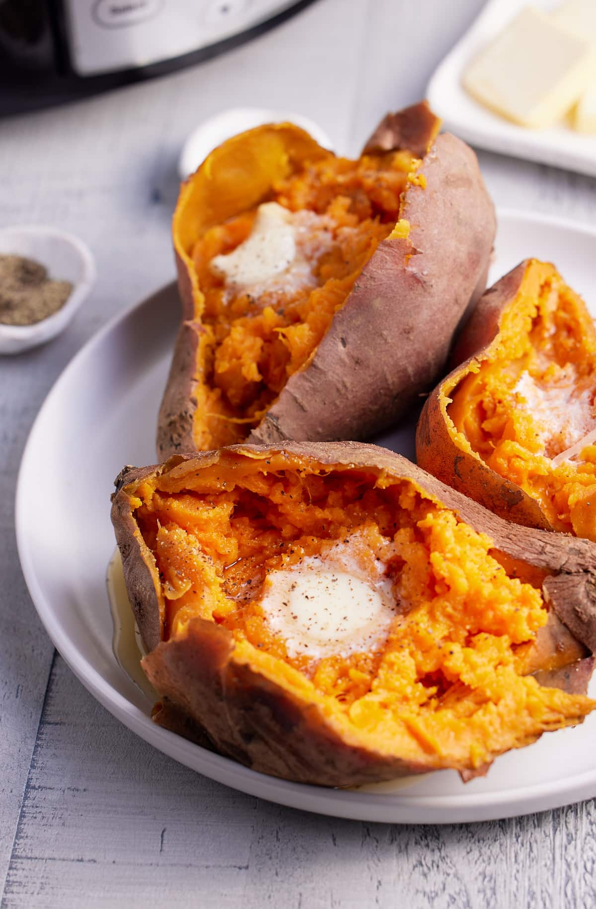 three cooked sweet potatoes on a plate topped with butter