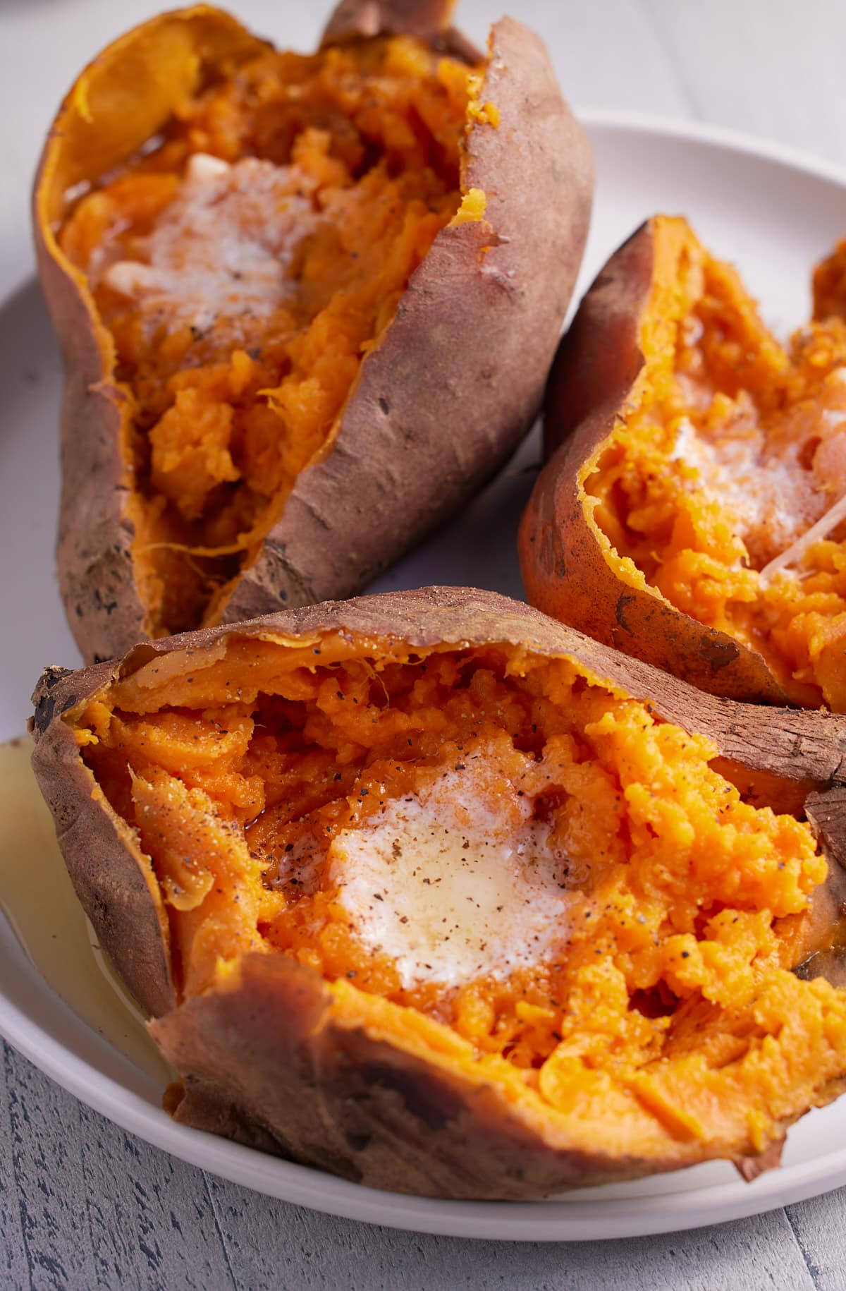 three cooked sweet potatoes on a plate topped with butter