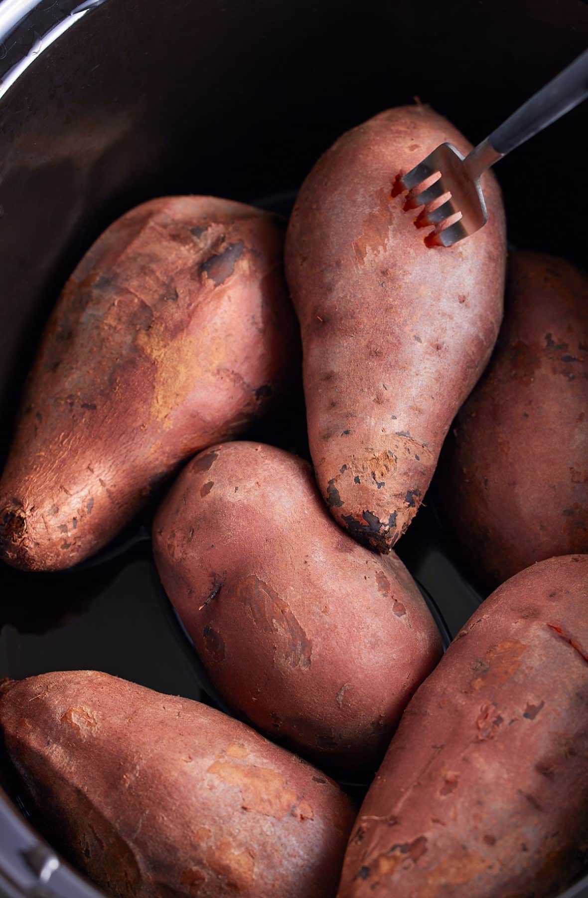 sweet potatoes in a slow cooker. a fork poking holes in them