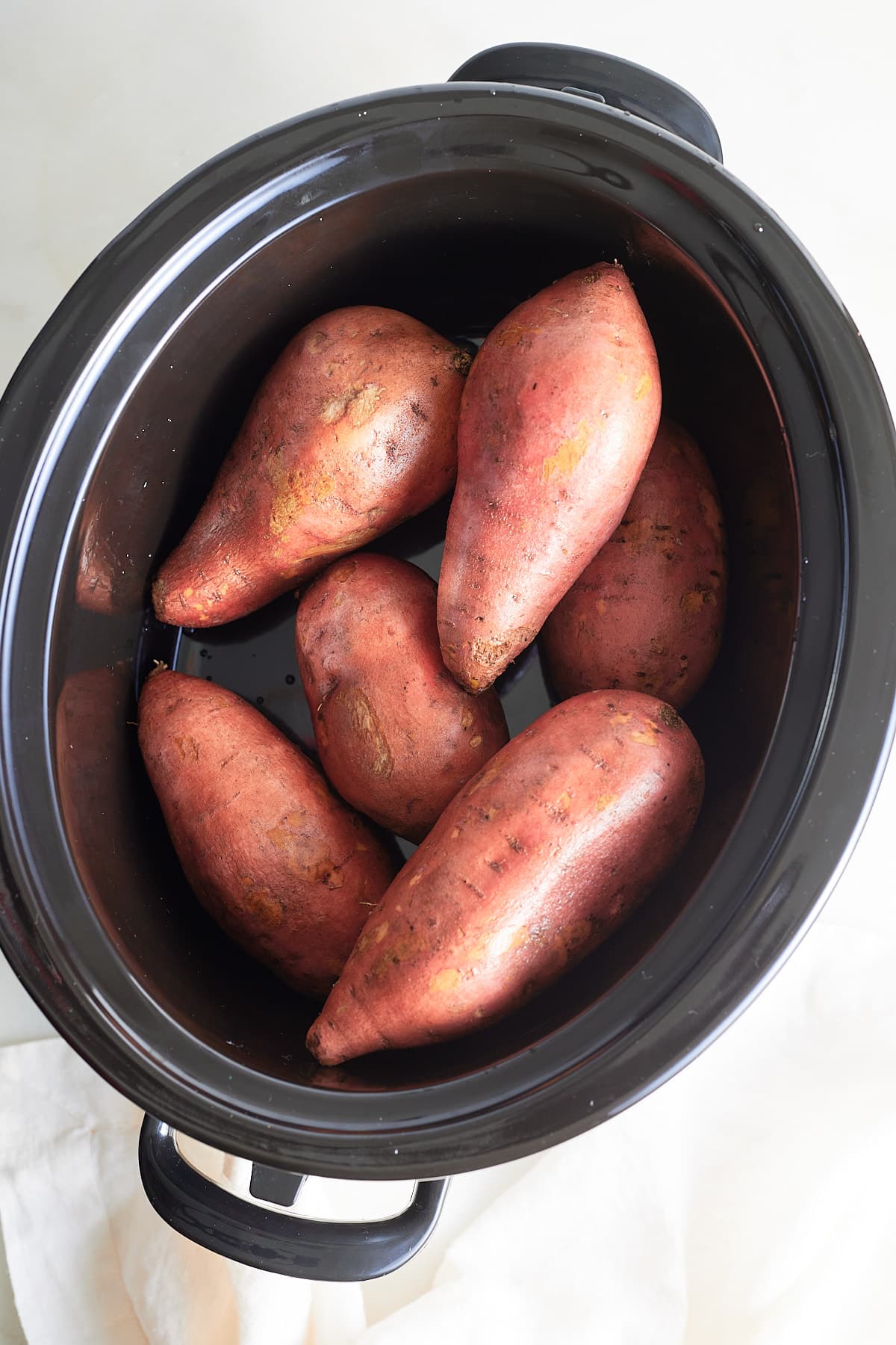 six whole sweet potatoes in a slow cooker