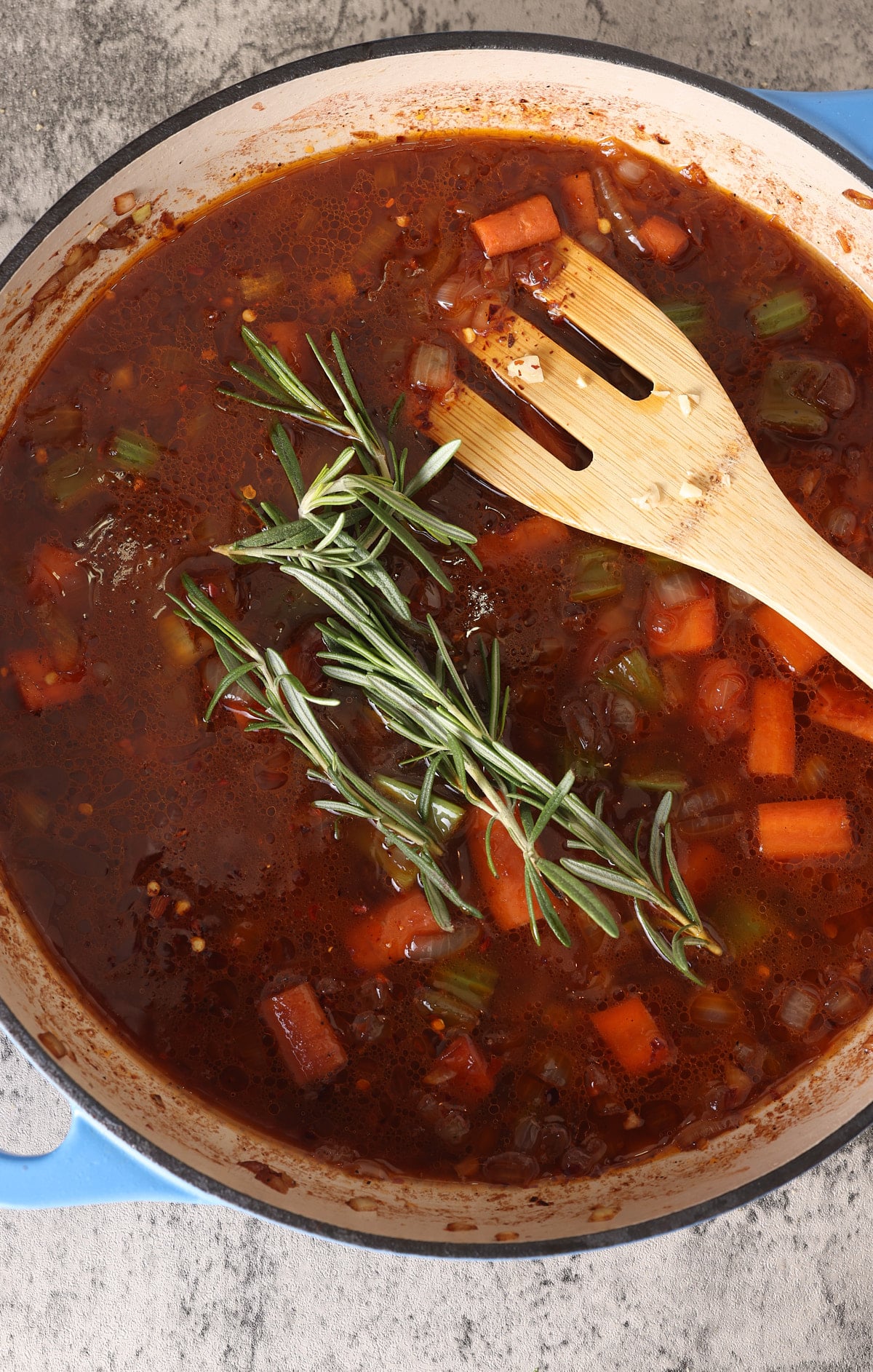 Dutch oven with sauteed vegetables and red wine and beef broth added topped with springs of fresh rosemary