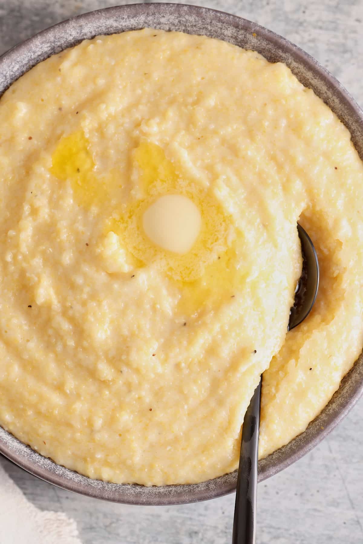 creamy polenta in a bowl with a spoon topped with butter, salt, and pepper.