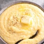 creamy polenta in a bowl with a spoon topped with butter, salt, and pepper.