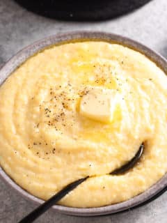 creamy polenta in a bowl with a spoon topped with butter, salt, and pepper.