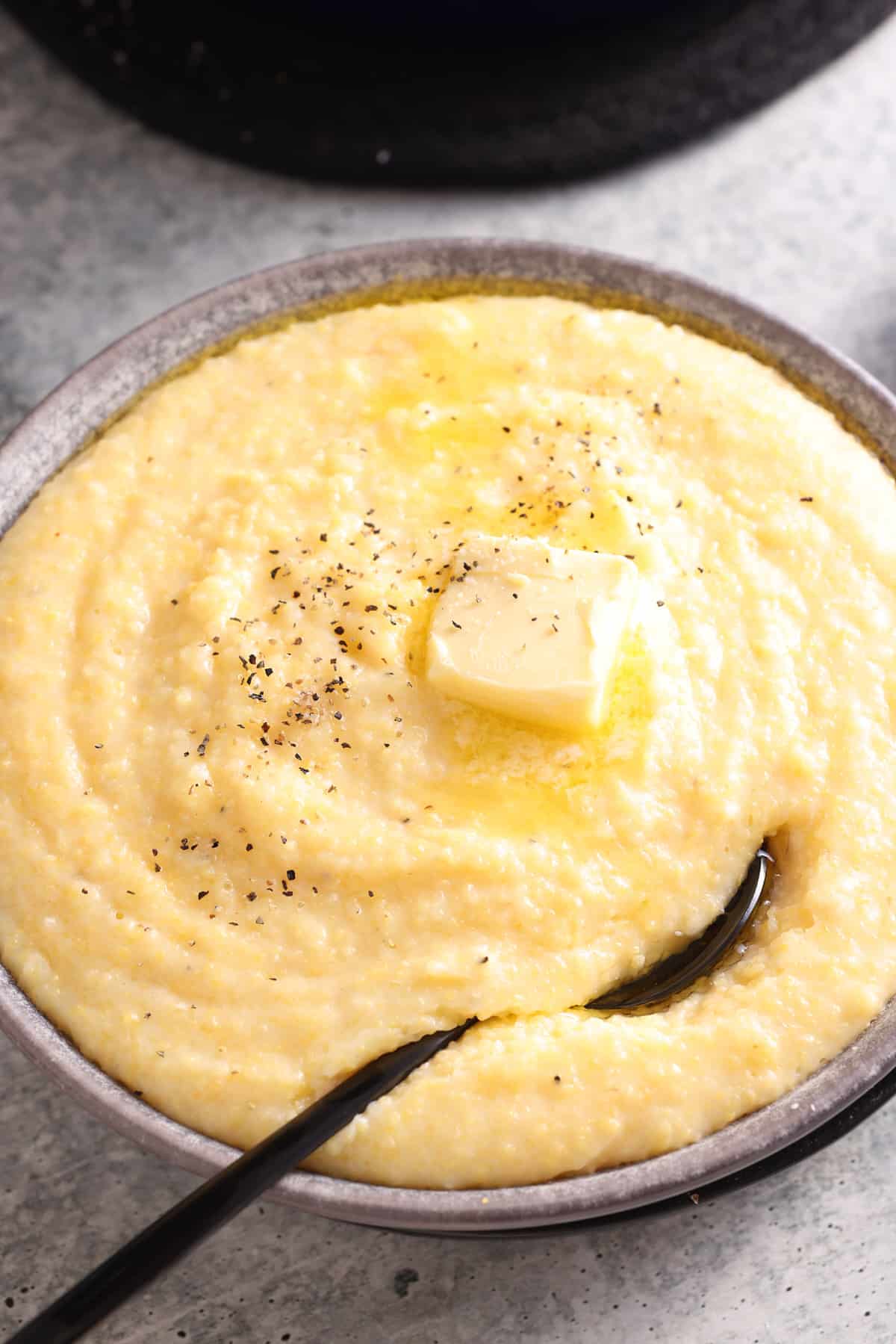 creamy polenta in a bowl with a spoon topped with butter, salt, and pepper.