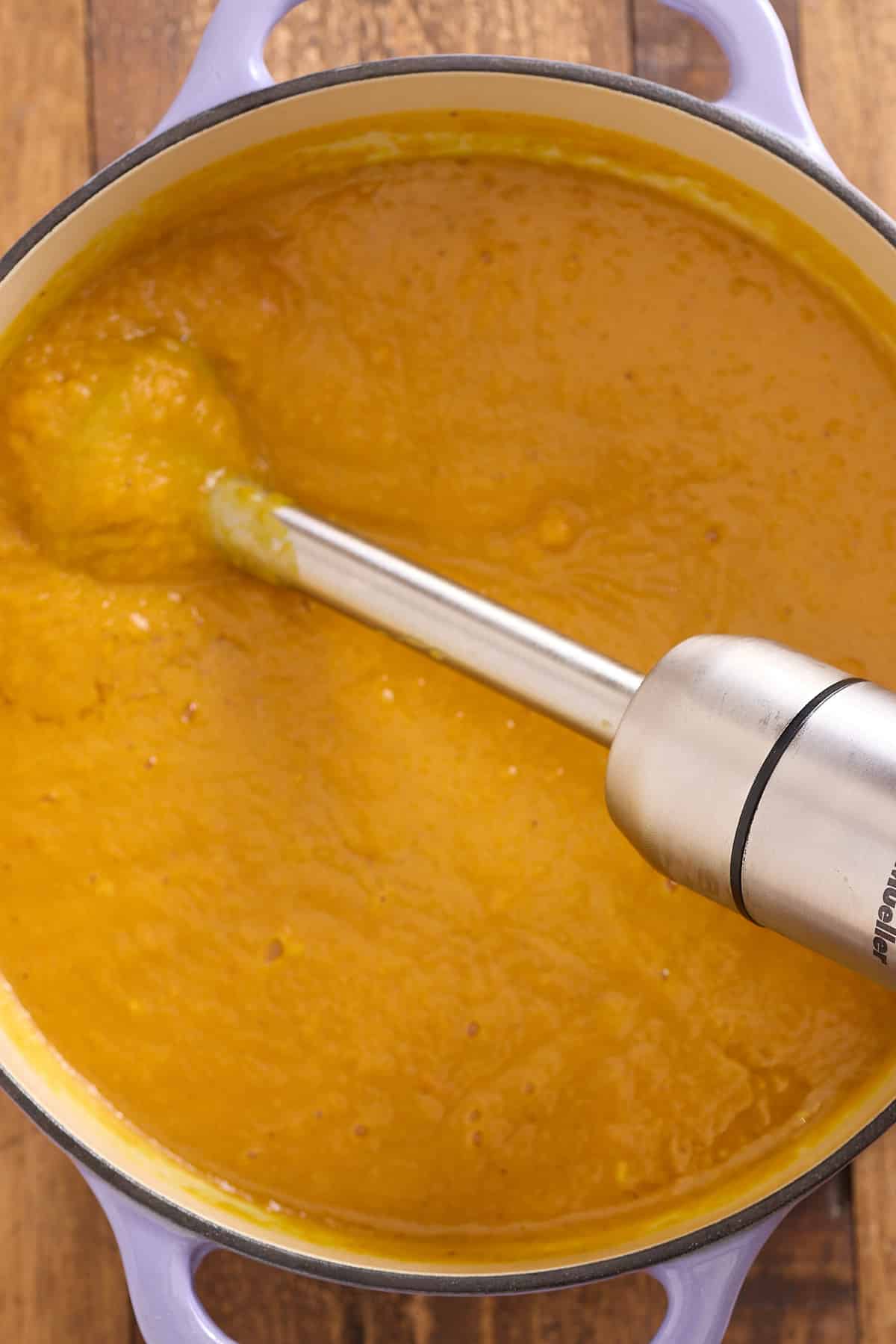 Dutch oven of sweet potato soup being blended using a stick blender