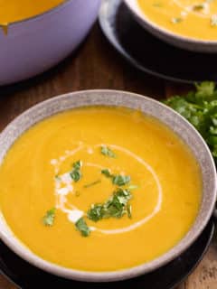 two bowls of sweet potato soup garnished with chopped cilantro and a drizzle of coconut milk