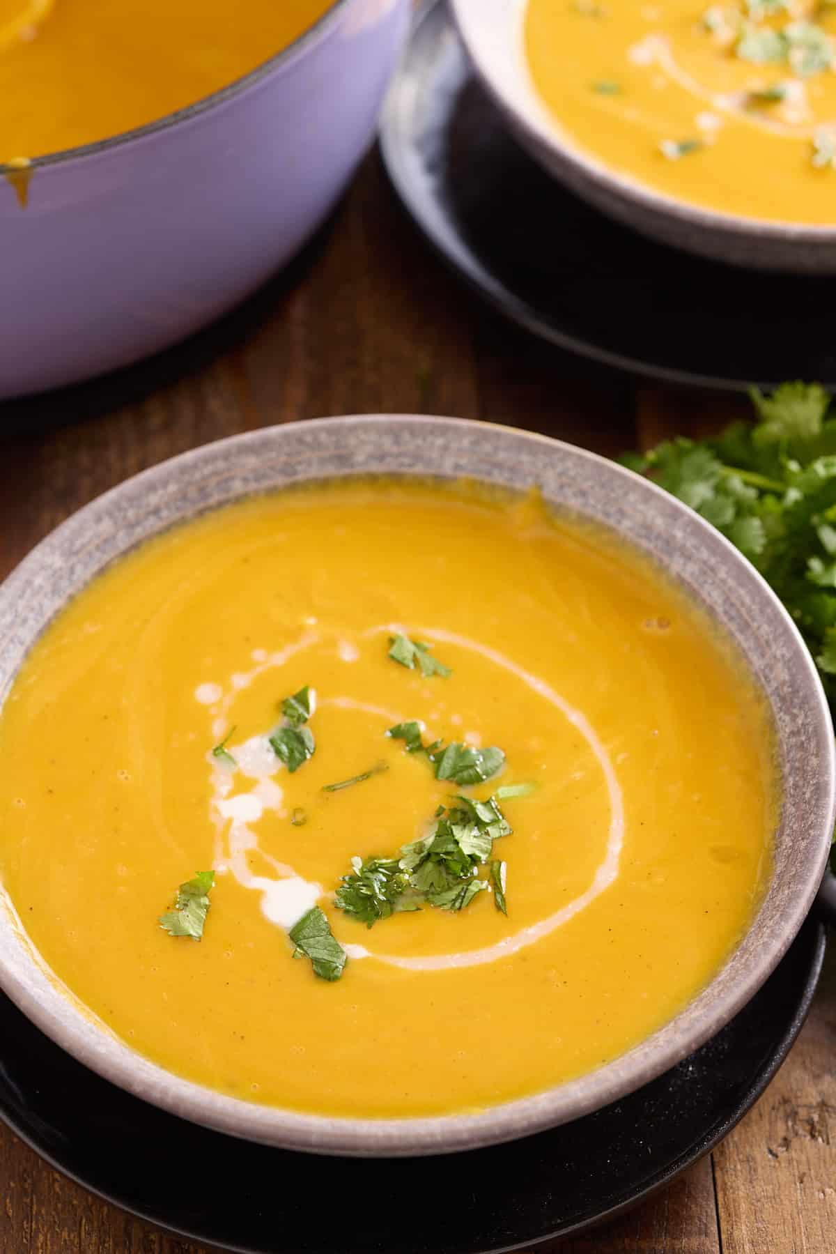 two bowls of sweet potato soup garnished with chopped cilantro and a drizzle of coconut milk
