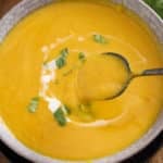 bowl of sweet potato soup garnished with chopped cilantro and a drizzle of coconut milk