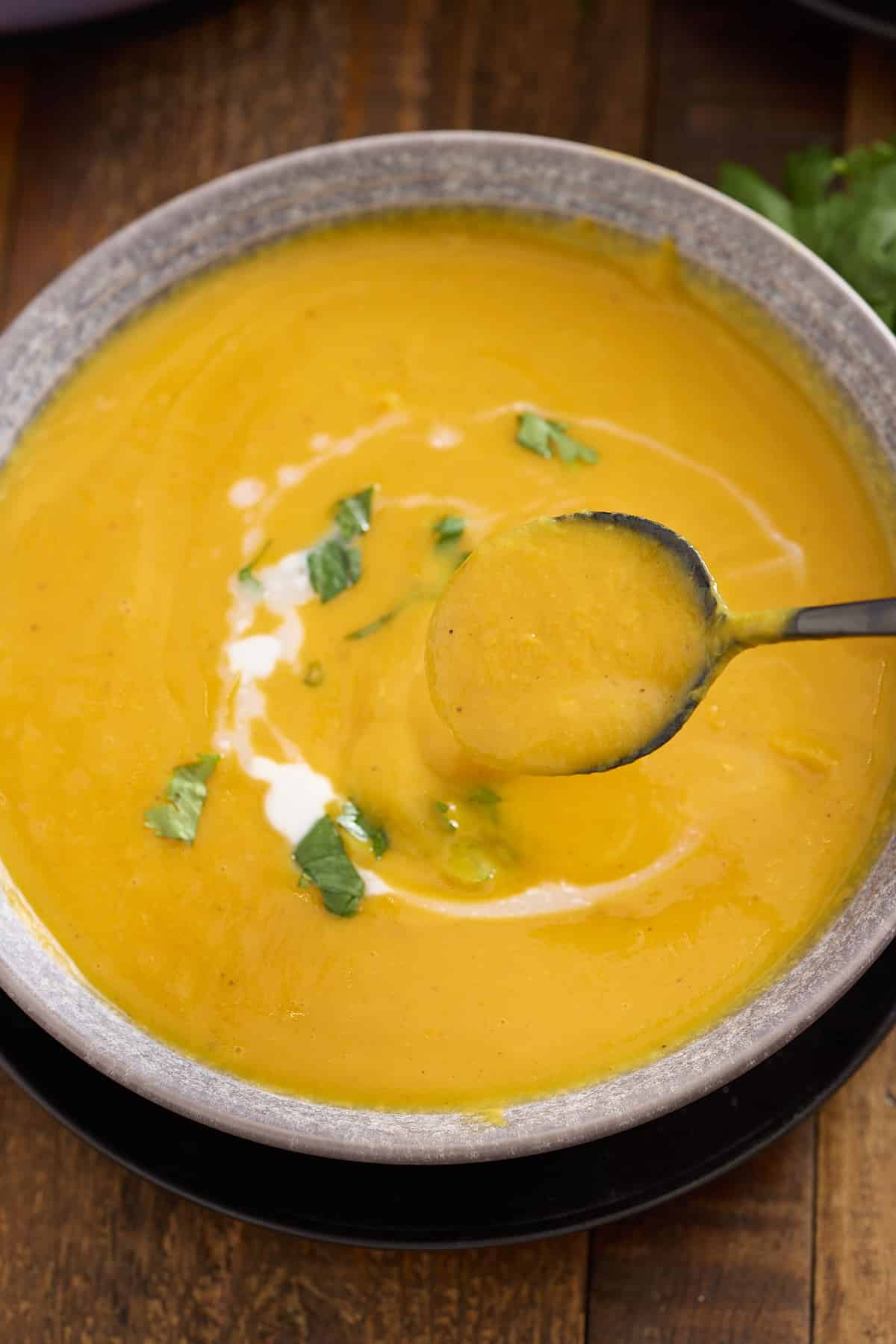 bowl of sweet potato soup garnished with chopped cilantro and a drizzle of coconut milk