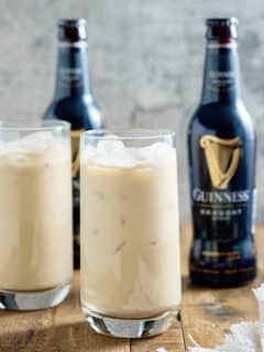 Two glasses filled with Jamaican Guinness punch served over ice with bottles of Guinness in the background