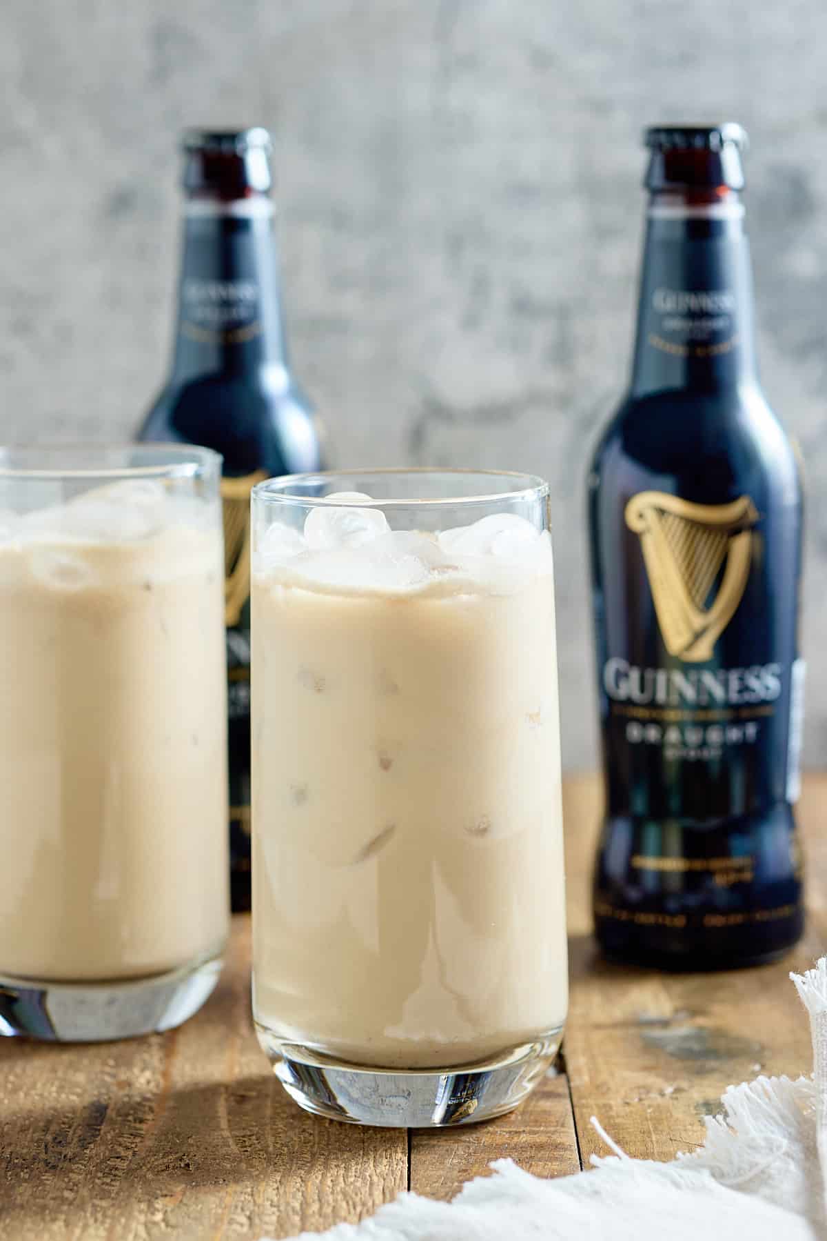 Two glasses filled with Jamaican Guinness punch served over ice with bottles of Guinness in the background