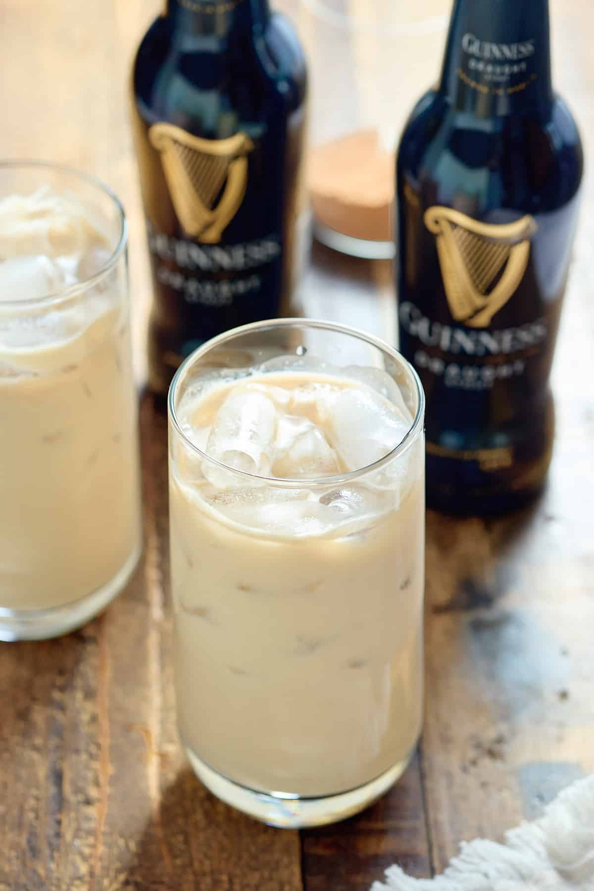 Two glasses filled with Jamaican Guinness punch served over ice with bottles of Guinness in the background