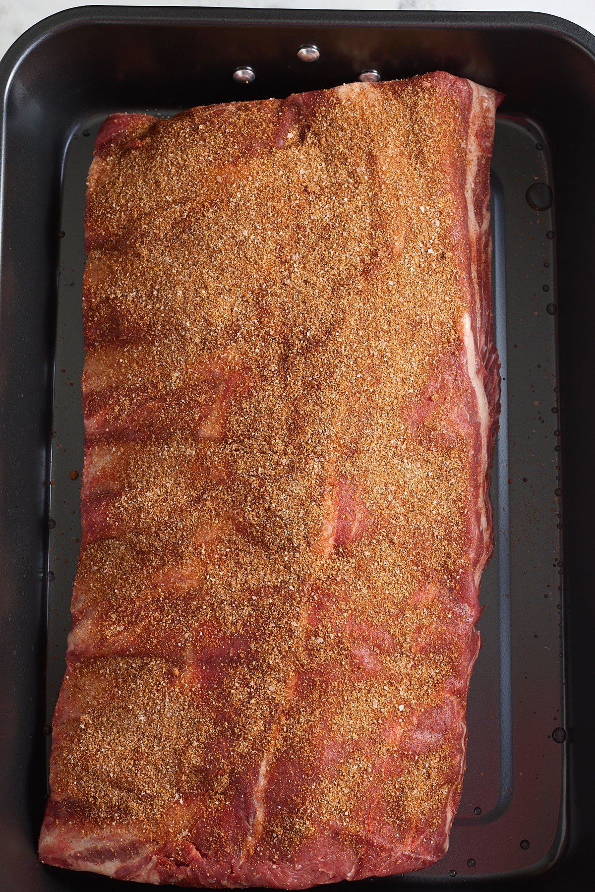 roasting pan with rack of beef ribs coated in bbq seasoning