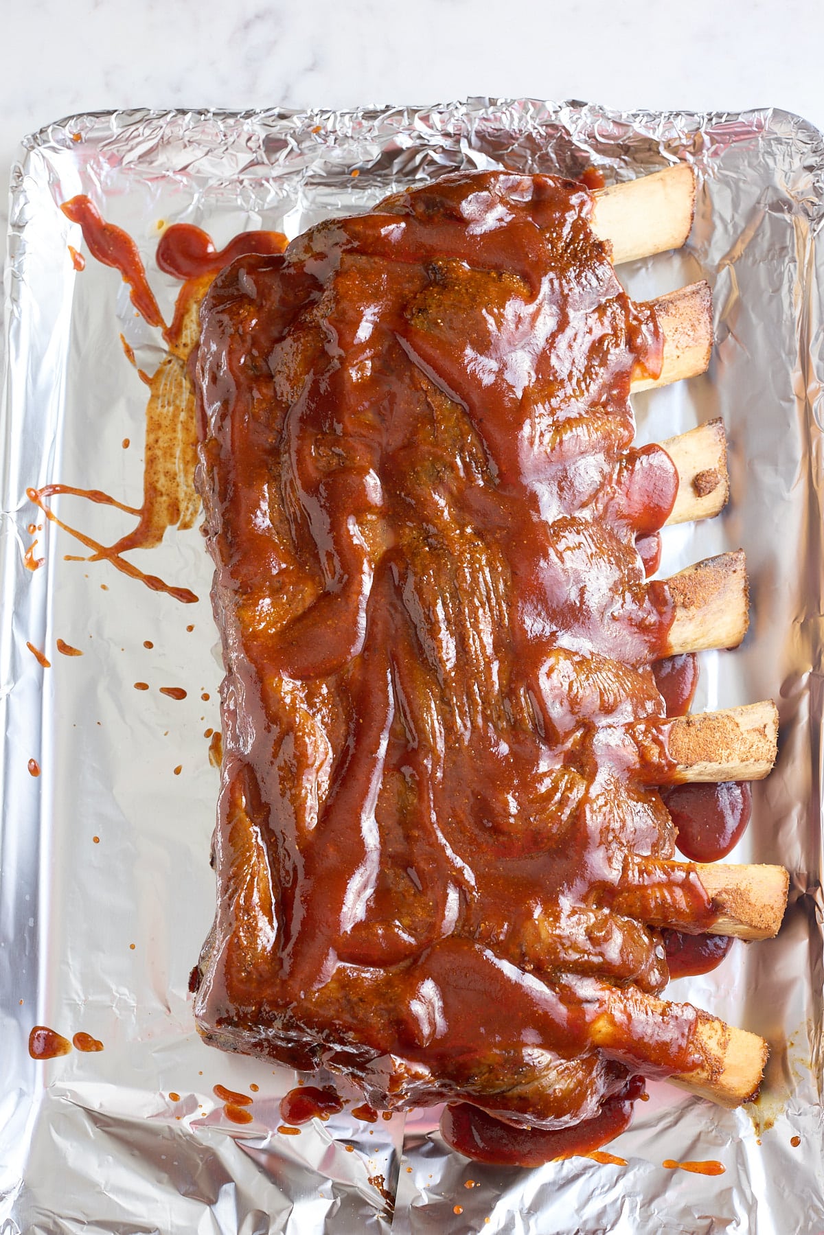 foil lined roasting pan with baked beef ribs coated in bbq sauce