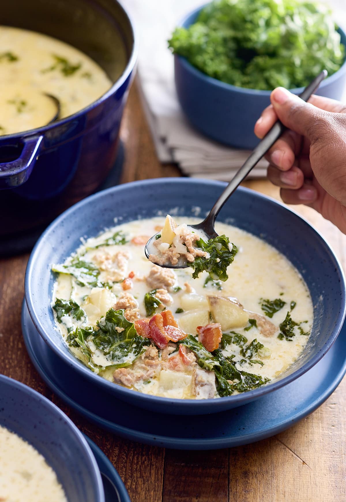 A bowl of zuppa toscana soup with someone take a bite with a spoon.