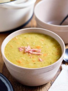 A bowl served with split pea soup topped with bits of ham.