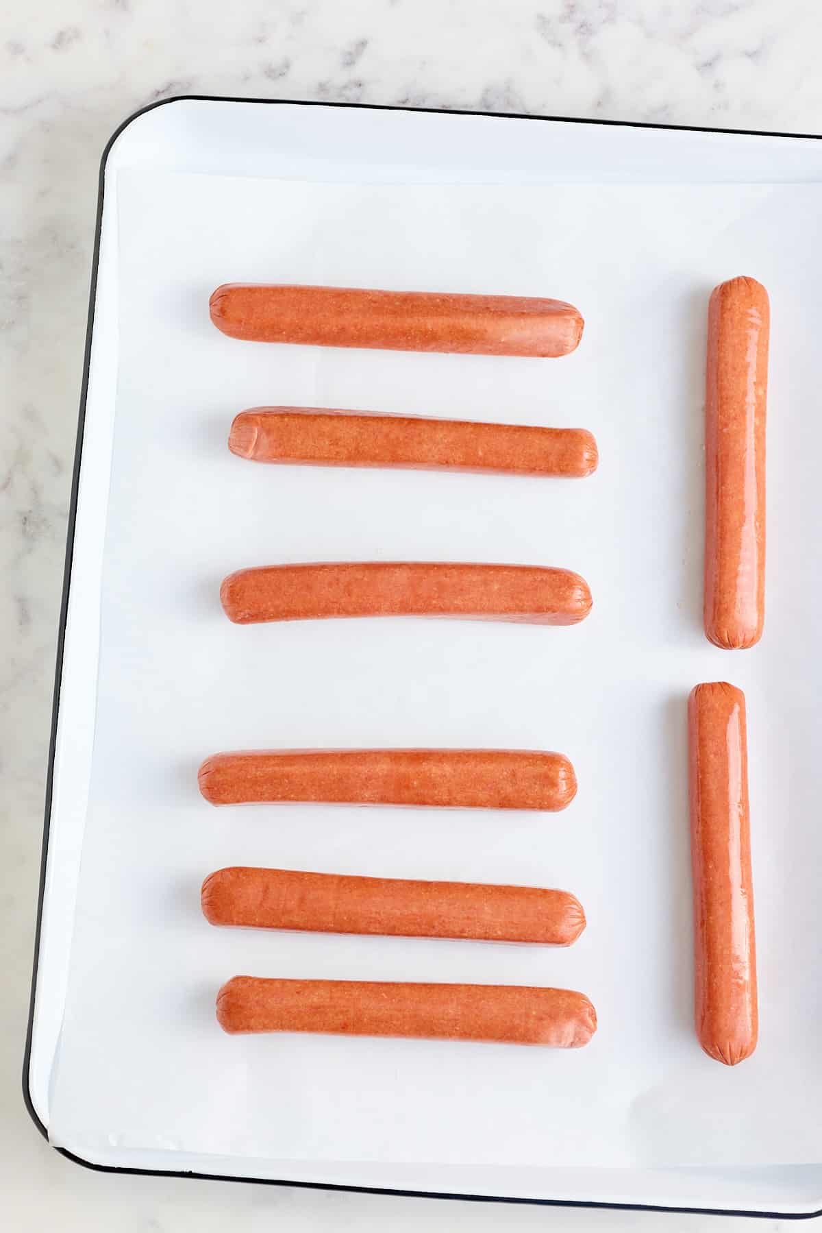 white baking sheet lined with baking parchment and hot dogs laid on top