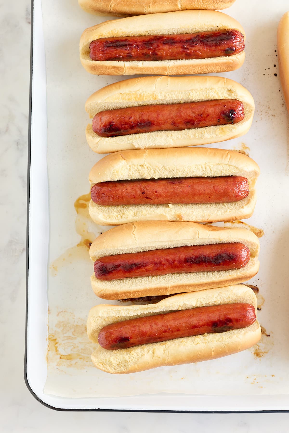 white baking tray with oven baked dogs in hot dog buns