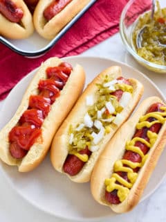 oven baked hot dogs in hot dog buns with a variety of toppings and sauces