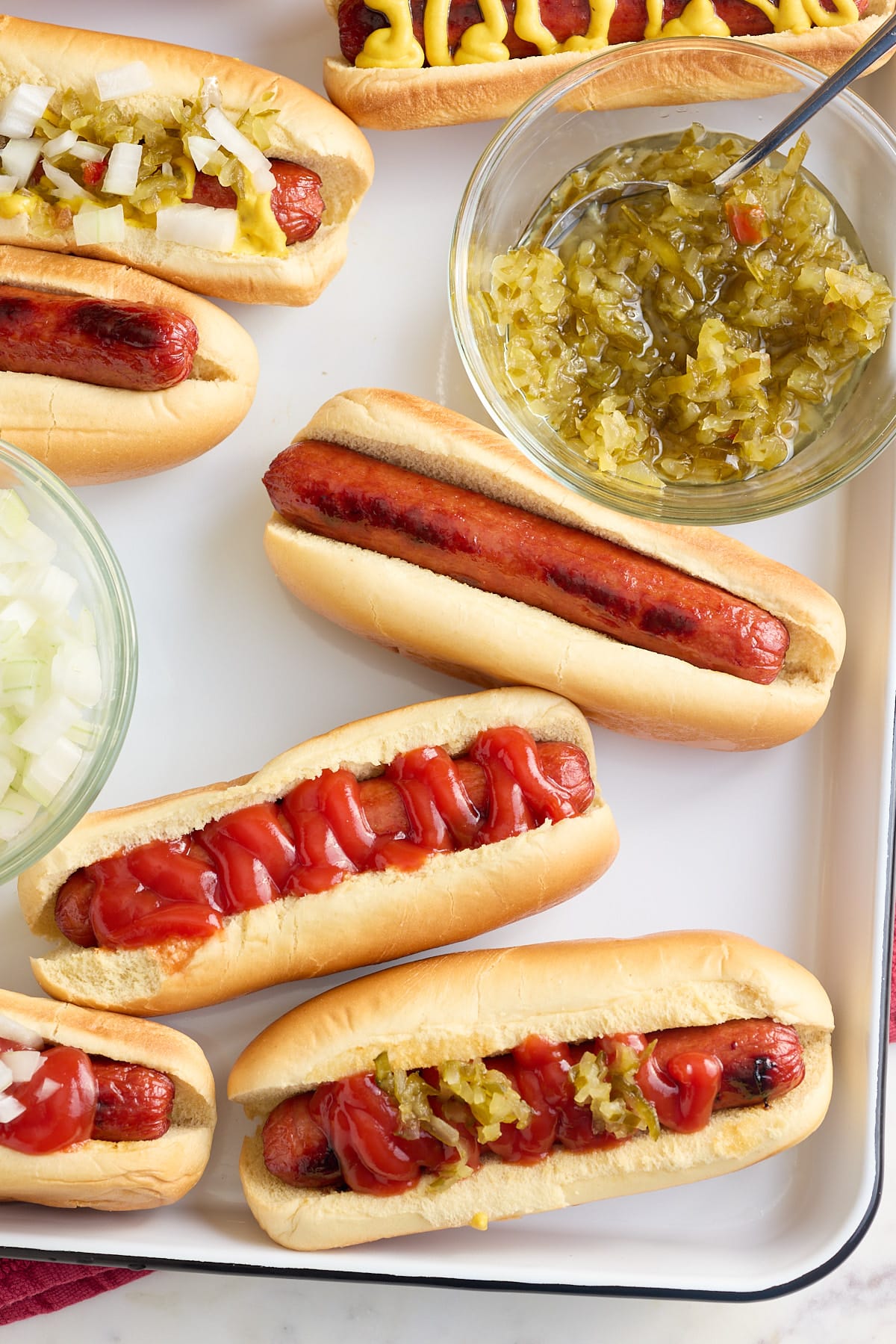 white tray with oven baked hot dogs in hot dog buns with a variety of toppings and sauces