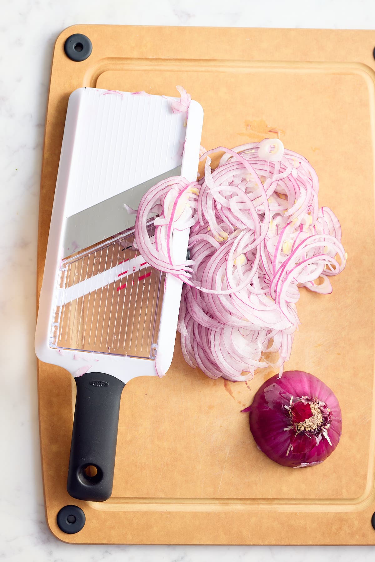 board with a mandolin, a red onion and a pile of finely sliced red onions